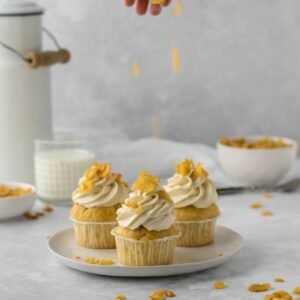 Vanilla cupcakes topped with frosting and cereal flakes, perfect sweet treat.